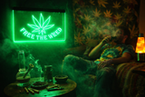 Person sitting in a dimly lit room with a neon sign reading 'Free the Weed' and smoking equipment on a table.