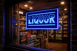 Blue “Liquor” LED sign hanging in a liquor store window at night, viewed from the street with shelves of bottles and beer cases visible inside the shop.
