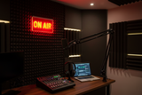 Radio studio setup with 'ON AIR' sign, laptop, and audio equipment.