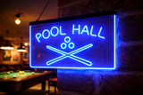 Neon sign reading 'Pool Hall' with pool cues and balls on a stone wall.