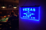 Glowing 'Texas Hold'em' sign in a dimly lit room with people playing poker.