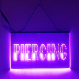 An LED sign with the word 'PIERCING' illuminated in purple, hanging from a metal chain.