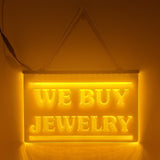 An LED sign with the text 'WE BUY JEWELRY' illuminated in yellow, hanging against a dark background.